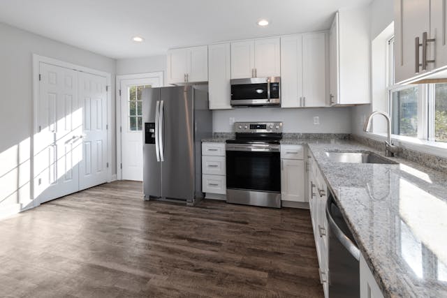 a kitchen with dark wood flooring and white cabinets and counters